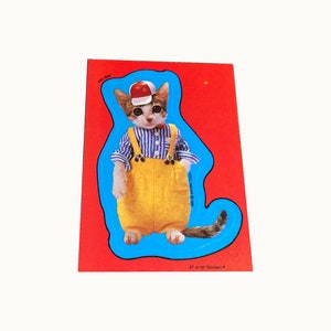 May include: A sticker featuring a cartoon cat wearing a blue and white striped shirt, yellow overalls, and a red baseball cap. The cat is standing on a blue background with a white outline. The sticker is part of a set of 56 stickers, and this is number 47.