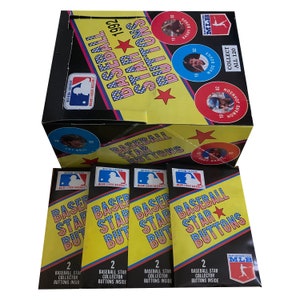 Peut inclure: Une boîte de boutons Baseball Star de 1992, avec un fond jaune et des étoiles rouges. La boîte présente une image d'un joueur de baseball sur le devant. Il y a quatre paquets de boutons sur la table, chacun avec un fond jaune et une étoile rouge. Les paquets indiquent "Baseball Star Buttons" et "2 Baseball Star Collector Buttons Inside".