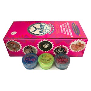 May include: A rectangular pink box labeled Slam Cans with graphics of characters and an eight ball, featuring text including Nova Ark, Balls O' Fire, and Jots Originals. Three translucent plastic containers in blue, green, and dark blue sit in front.