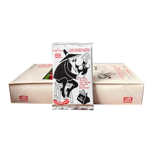 May include: A sealed card pack with a black and white cartoon character illustration. The pack is silver with text that reads "LOOK FOR SPECIAL BONUS CARDS RANDOMLY INSERTED". A box of cards is in the background.