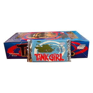 Puede incluir: Una caja azul y roja de cromos de Tank Girl con un paquete envuelto en papel de aluminio en frente. El paquete presenta un gráfico de tanque verde y las palabras "TANK GIRL" en rojo. La caja dice "10 cartas por paquete, 48 unidades."
