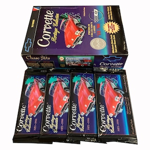 May include: A box set of Corvette Heritage Collection trading cards. The box features a red Corvette and the text "Corvette Heritage Collection." Several packs of cards are visible, each with a red Corvette image and the text "1953-1996."