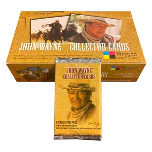 May include: A box of John Wayne Collector Cards with a pack of cards in front. The box is light brown with images of John Wayne and the text "JOHN WAYNE COLLECTOR CARDS". The pack has an image of John Wayne and the text "6 CARDS PER PACK".