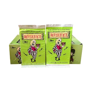 Könnte beinhalten: Zwei Packungen Beetlejuice-Sammelkarten mit grünem Hintergrund und den Aufschriften "The Ghost With The Most!" und "Beetlejuice". Die Packungen zeigen ein Cartoon-Bild von Beetlejuice. Eine Box mit dem gleichen Design befindet sich hinter den Packungen.