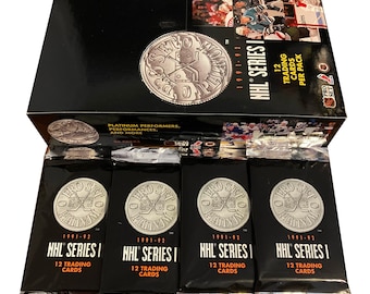May include: A box of 1991-92 Pro Set NHL Series 1 hockey trading cards. The box contains four packs of cards, each with 12 cards. The box is black with a silver coin design featuring a hockey stick and puck. The text "Pro Set Platinum" is printed on the coin. The box also features the text "1991-92 NHL Series I" and "12 Trading Cards Per Pack".