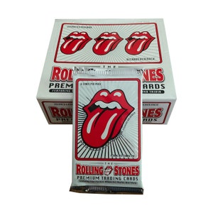 May include: A box of The Rolling Stones Premium Trading Cards featuring the iconic red tongue logo. The box displays the logo and text, with a pack of cards in front. Each pack contains 6 cards, and the box contains 24 packs.