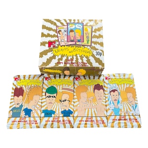May include: A box of 1994 Inaugural Edition Beavis and Butt-Head collector cards with gold foil accents. Several unopened packs of cards are displayed in front of the box, each featuring different cartoon images of the characters.