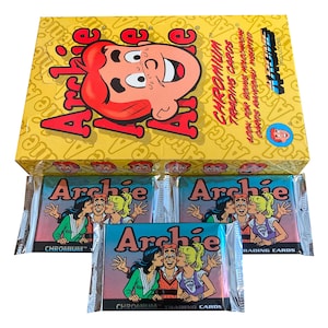 May include: A yellow box of Archie comic book trading cards featuring the Archie Comics logo and character illustrations. The box reads "Chromium Trading Cards." Below are three sealed packs of cards with Archie characters kissing.