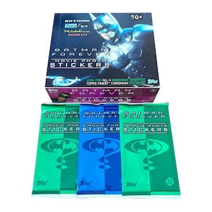May include: A box of "Batman Forever" movie photo stickers with three unopened packs. The box features Batman and the text "Batman Forever." The sticker packs are green and blue with the Batman logo.