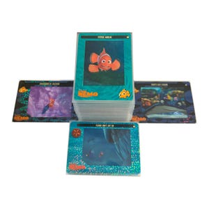 May include: A stack of Finding Nemo trading cards featuring images from the animated film. The top card shows Nemo, an orange and white clownfish, with the text "FATHER MARLIN". Other cards display underwater scenes and characters.