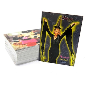 May include: A stack of trading cards featuring images from the TV show "Sabrina the Teenage Witch." One card is displayed, showing Sabrina in a black dress and witch hat, with the text "Mystical Trading Cards."
