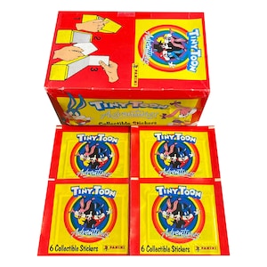 May include: A box of Tiny Toon Adventures collectible stickers. The box is red with a white border and features the Tiny Toon Adventures logo. The stickers are in four packs, each with a different Tiny Toon character. The packs are yellow with a rainbow border and feature the Tiny Toon Adventures logo.