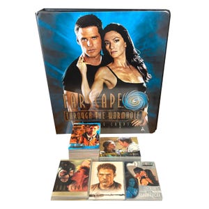 Op de afbeelding: Een Farscape-verzamelkaartenbinder met een blauwzwarte omslag met twee personen. Er zijn verschillende verzamelkaarten zichtbaar, met verschillende scènes en personages uit de Farscape-serie. De tekst "Farscape Through the Wormhole" staat op de binder.