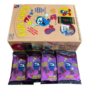 May include: A box of "Fun Caps" collectible game pieces with a cartoon character illustration. The box features the text "Fun Caps" and "Olympic Games Collection". Below are four packs of "Slammers" with the same cartoon character.