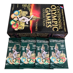 May include: A box of Centennial Olympic Games Collection trading cards, Volume 1. The box is black with gold lettering and features a red and yellow image of the Olympic rings and a figure running. The box is open and shows five packs of cards, each with a green background and the Olympic rings.