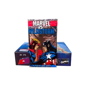 May include: A pack of Marvel vs. Wildstorm trading cards, with Captain America and another superhero on the front. The pack is in front of a box of cards, with the text "MARVEL VS WILDSTORM TRADING CARDS".