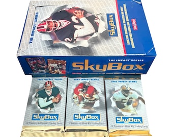 May include: A SkyBox trading card box set with three unopened packs. The box is blue and white with the words "SkyBox" and "The Impact Series." The packs are silver and gold with images of football players.