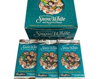 May include: A box of SkyBox trading cards featuring Snow White and the Seven Dwarfs. The box is turquoise blue with a picture of Snow White and the Seven Dwarfs on the front. The box is surrounded by three packs of trading cards, each with a picture of Snow White and the Seven Dwarfs on the front. The packs are silver and blue with the words "Snow White and the Seven Dwarfs" printed on them.