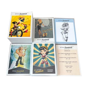 May include: A collection of DC Comics Bombshells trading cards. The cards feature various female characters in vintage-inspired pin-up style artwork. The cards include characters like Wonder Woman and Black Canary. A checklist is also included.