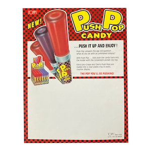 May include: A vintage advertisement for Push Pop candy. The ad features a red and purple Push Pop candy stick with the text "Push Pop Candy" and "Push It Up and Enjoy!" The ad also features a display of Push Pop candy sticks in a clear plastic tray.