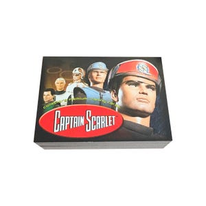 Puede incluir: Una pila de cartas de intercambio de Captain Scarlet con un grupo de personajes del programa. Los personajes llevan uniformes futuristas y la carta presenta el logotipo del programa.