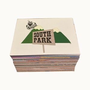 May include: A stack of trading cards featuring the "South Park" logo and Comedy Central branding. The top card displays the show's signpost with the text "SOUTH PARK" and green mountain graphics. The cards have colorful edges.