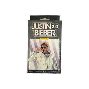 May include: A black trading card box with the words "JUSTIN 2.0 BIEBER" in white and grey. The box features an image of Justin Bieber wearing sunglasses and holding a microphone. The box reads "36 CARDS PER BOX" and has the Panini logo.