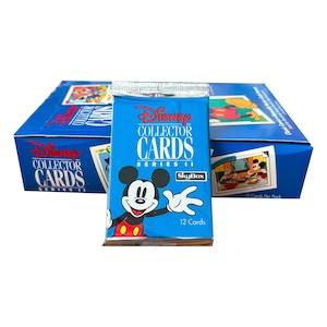 Op de afbeelding: Een blauwe doos met Disney Collector Cards Serie II met een pakje kaarten ervoor. Het pakje toont Mickey Mouse en de tekst "Disney Collector Cards Serie II". De doos heeft ook het Disney-logo en de tekst "12 kaarten per pakje".
