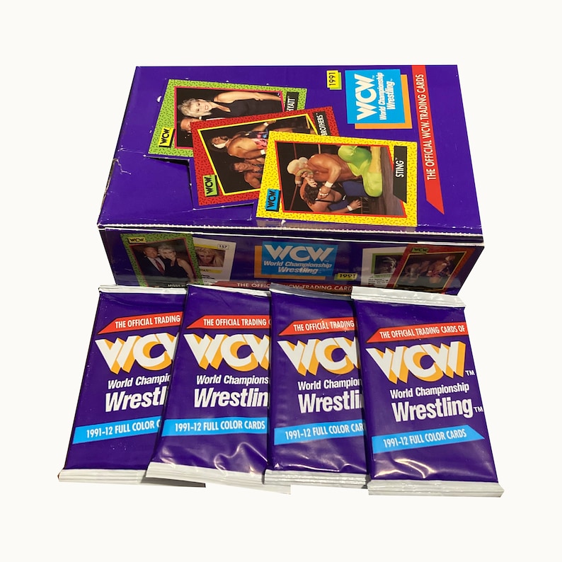 K&ouml;nnte beinhalten: Eine Schachtel mit WCW World Championship Wrestling Sammelkarten aus dem Jahr 1991. Die Schachtel ist lila mit gelbem Rand und zeigt ein Bild von Sting auf der Vorderseite. Die Schachtel ist von f&uuml;nf Sammelkartenpackungen umgeben, die jeweils einen lila Hintergrund und das WCW-Logo haben.