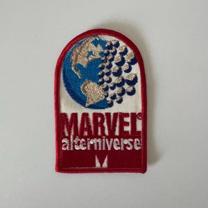 May include: Embroidered patch with a red border and the text "MARVEL altermiverse". The patch features a blue and gold globe design with a cluster of blue shapes. The patch is rectangular with a rounded top.