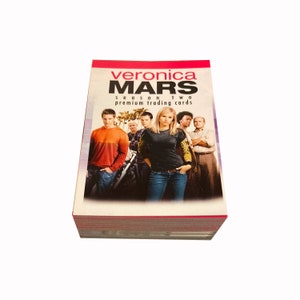 May include: A stack of "Veronica Mars" Season Two premium trading cards. The card packaging features a group of people, with the show's title in red and black text at the top. The cards have a red border.