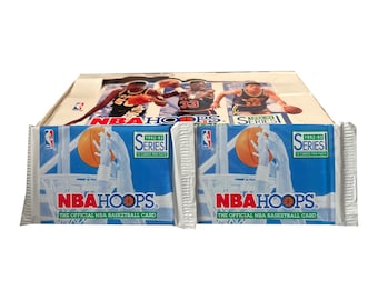 May include: A display box of 1992-93 NBA Hoops Series 1 basketball cards featuring two sealed packs in the foreground. The packaging is blue and white with a graphic of a basketball and hoop, labeled with the NBA Hoops logo and text.