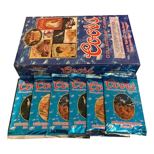 May include: A box set of Coors Collector's Cards with multiple packs of cards. The box is blue with the Coors logo and various images. The packs are blue with the Coors logo and the words "Collector's Cards".