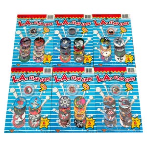 May include: Multiple packs of L.A. Slap Caps, each with a unique design. The packs feature a variety of colorful, collectible slap caps with different graphics, including skulls, yin-yang symbols, and other illustrations. Each pack contains six caps.