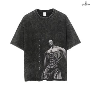 Puede incluir: Camiseta gris oscuro con efecto lavado desgastado. Presenta un gráfico de una figura esquelética con músculos expuestos. Texto japonés impreso verticalmente en el lado izquierdo del gráfico.