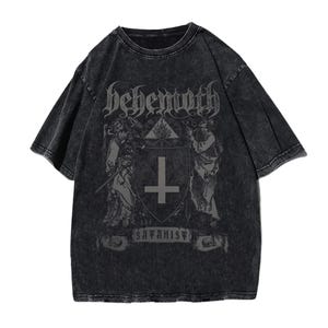 May include: Dark grey t-shirt with a distressed finish. The front displays the word "Behemoth" in gothic lettering above a graphic of a shield with a cross and figures. The text "the Satanist" is below the shield.