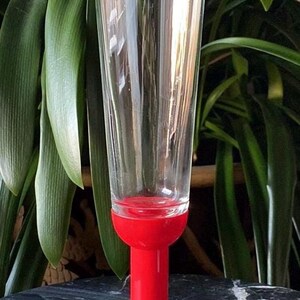 May include: A red stemmed glass with a clear glass bowl. The glass is on a black marble surface.