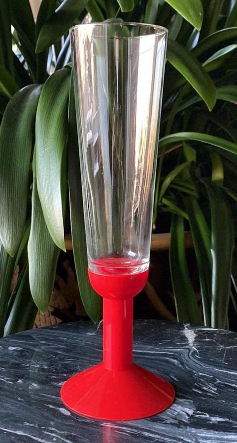 May include: A red stemmed glass with a clear glass bowl. The glass is on a black marble surface.
