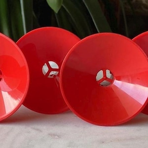 May include: Four bright red plastic funnels with a small hole in the center of each. The funnels are all the same size and shape.