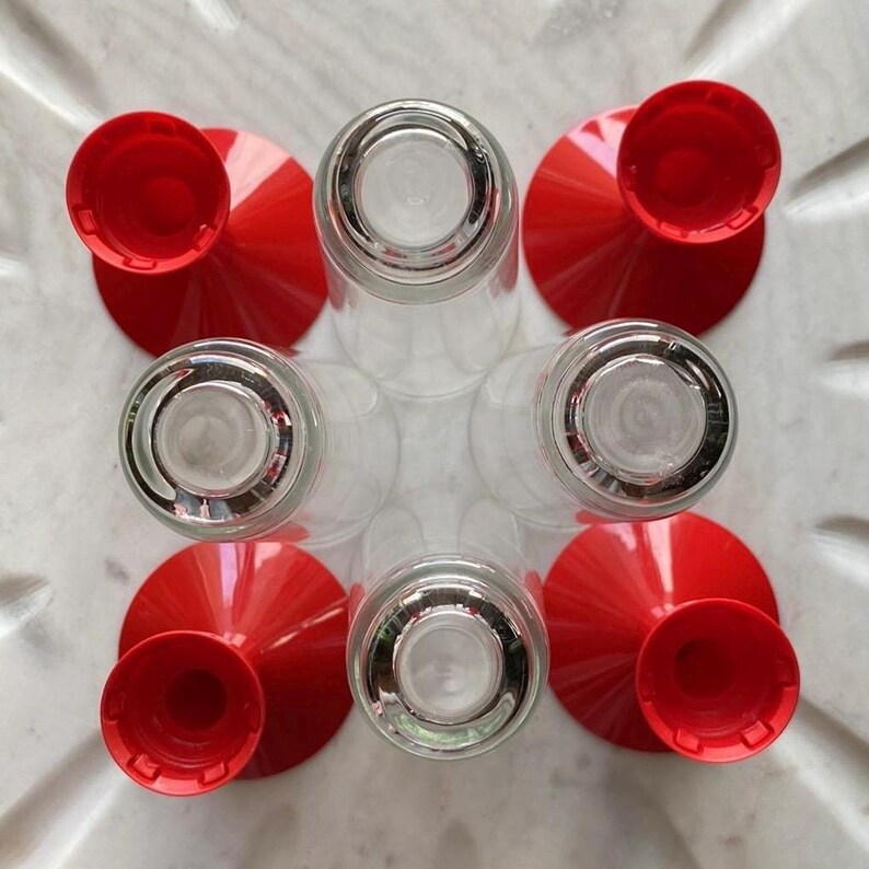 May include: Six clear glass shot glasses with red plastic bases. The bases are shaped like cones with a round opening at the top.