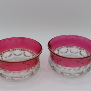 May include: Two clear glass bowls with a red rim. The bowls have a pattern of small circles around the rim and bottom.
