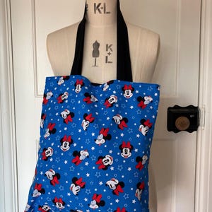 May include: A blue tote bag with a white star and red and black Minnie Mouse print. The bag has black straps.