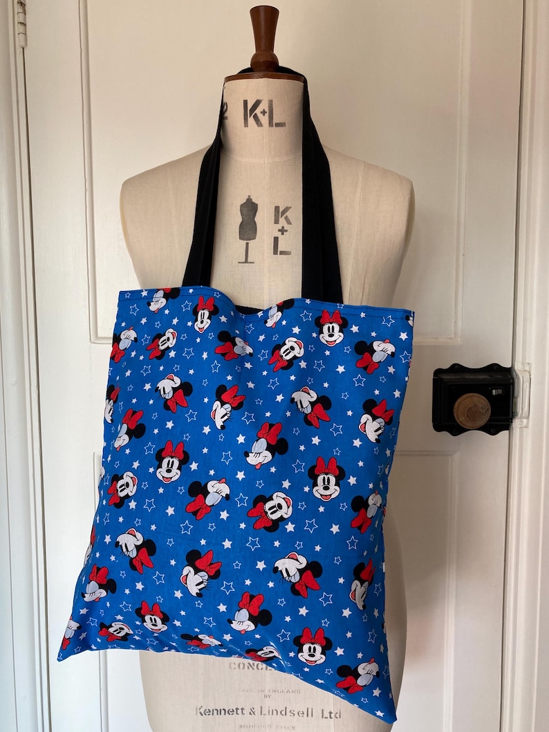 May include: A blue tote bag with a white star and red and black Minnie Mouse print. The bag has black straps.