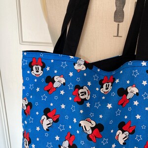 May include: A blue tote bag with a white star and Minnie Mouse pattern. The bag has black straps.