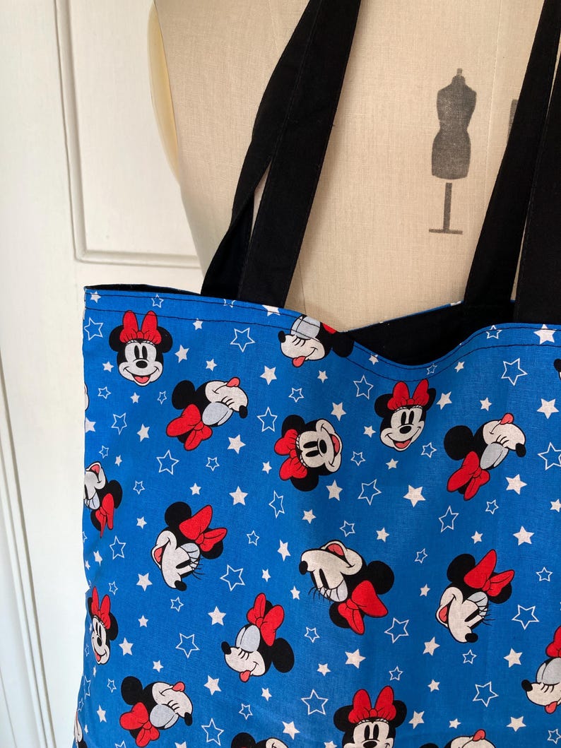 May include: A blue tote bag with a white star and Minnie Mouse pattern. The bag has black straps.