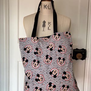 May include: A gray tote bag with a black handle and a repeating pattern of Mickey Mouse heads in red, black, and white on a gray background with red and white confetti.