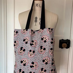 May include: A gray tote bag with black straps featuring a repeating pattern of Mickey Mouse heads in red, black, and white on a gray background with red and blue confetti.