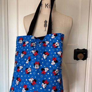 May include: A blue tote bag with a white star and Minnie Mouse print. The bag has black straps.