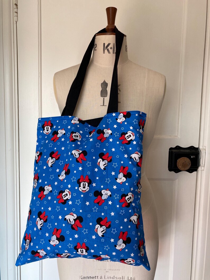 May include: A blue tote bag with a white star and Minnie Mouse print. The bag has black straps.