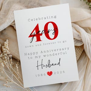 Könnte beinhalten: Eine weiße Jubiläumskarte mit dem Text "Celebrating 40 years" in Rot und Schwarz. Die Karte enthält auch den Text "Happy Anniversary to my wonderful Husband" und die Jahre 1986-2026.